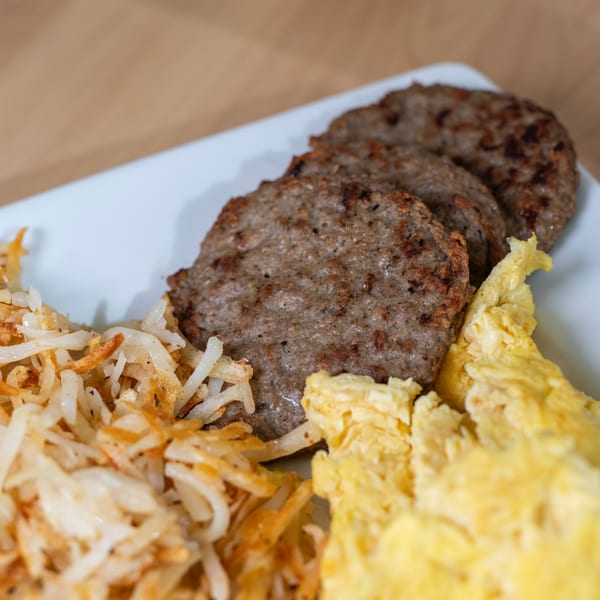 A brunch plate with three sausage patties, hash browns, and scrambled eggs.