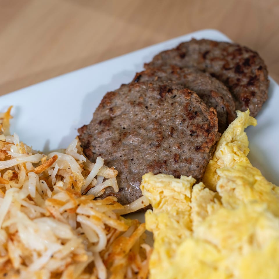 A brunch plate with three sausage patties, hash browns, and scrambled eggs.