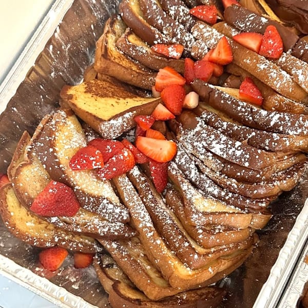 A large tray of French toast, dusted with powdered sugar and topped with fresh strawberries.