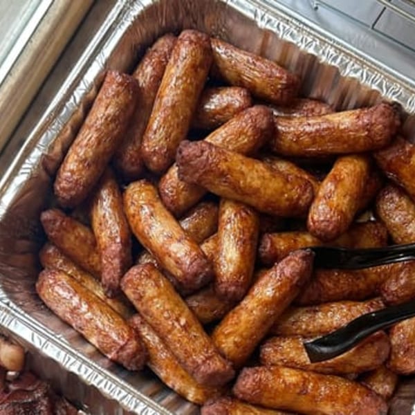 A foil pan filled with many browned breakfast sausage links, ready for a brunch buffet.