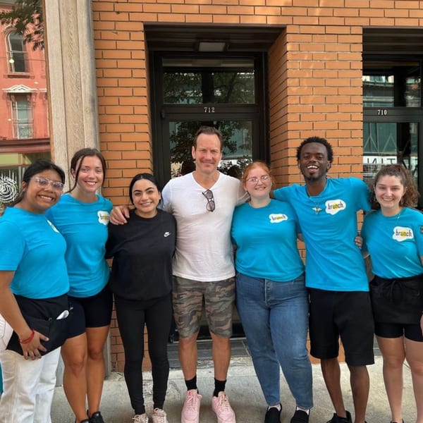 Seven smiling Brunch. staff members, wearing blue shirts, pose together outside the restaurant.