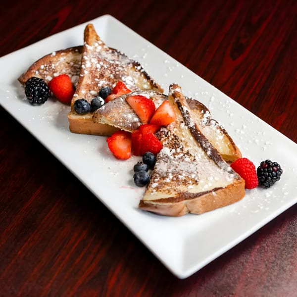 French toast triangles dusted with powdered sugar, topped with fresh strawberries, blueberries, and blackberries.