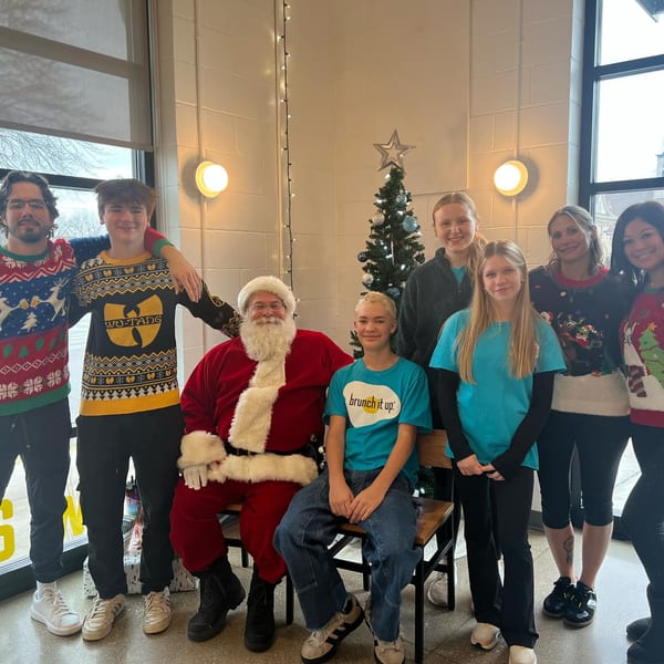 Santa Claus sits with Brunch It Up staff and guests in festive holiday sweaters.