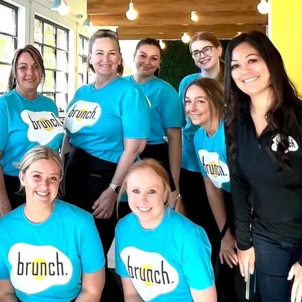 Eight smiling female Brunch. restaurant staff members in blue and black branded shirts.