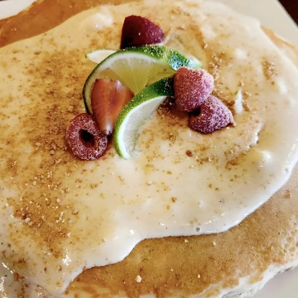 Close-up of pancakes with cream, lime slices, and raspberries, sprinkled with brown sugar.