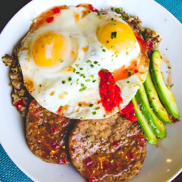 A brunch plate with two fried eggs, two sausage patties, avocado slices, and quinoa.