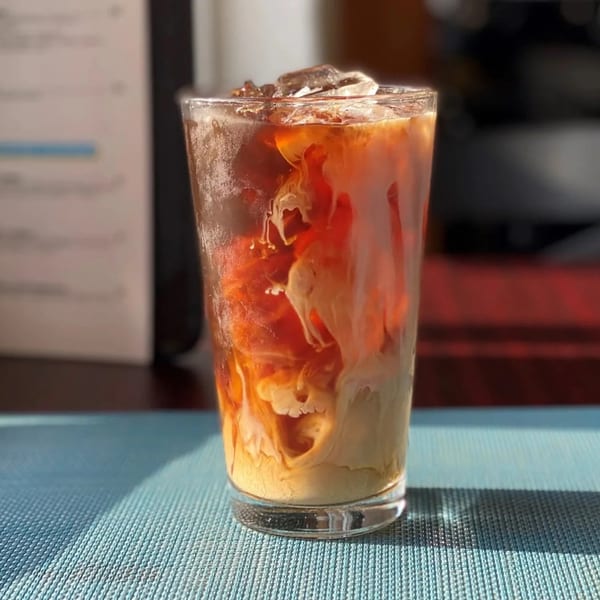 Iced coffee with cream swirling into the dark liquid, on a blue placemat.