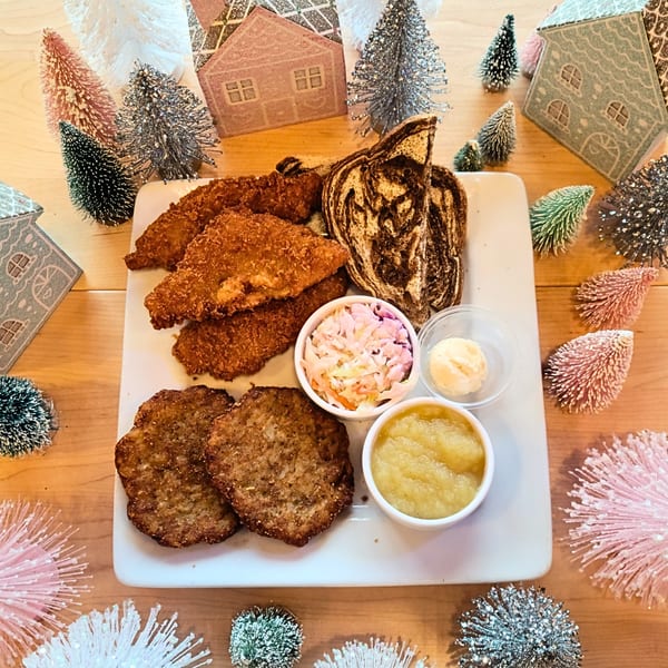 Brunch plate with fried chicken, sausage patties, marble rye, coleslaw, applesauce, and butter.
