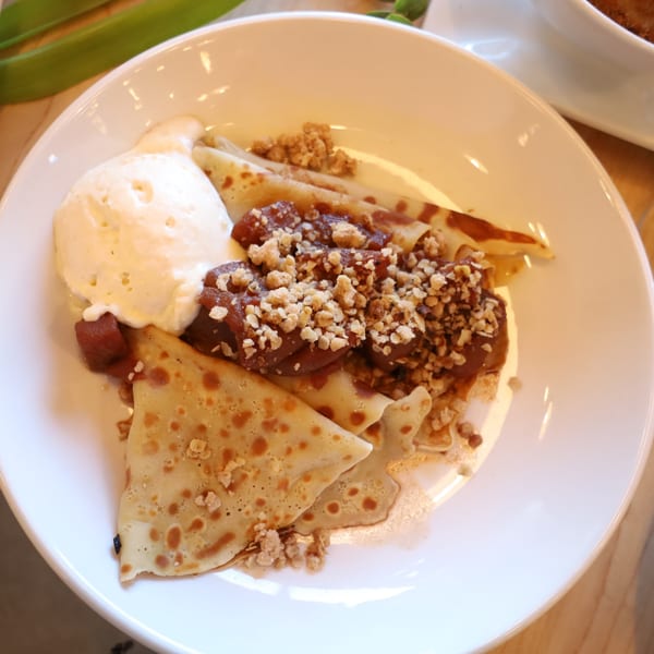 Brunch crepes with caramelized apples, ice cream, and crunchy topping on a white plate.