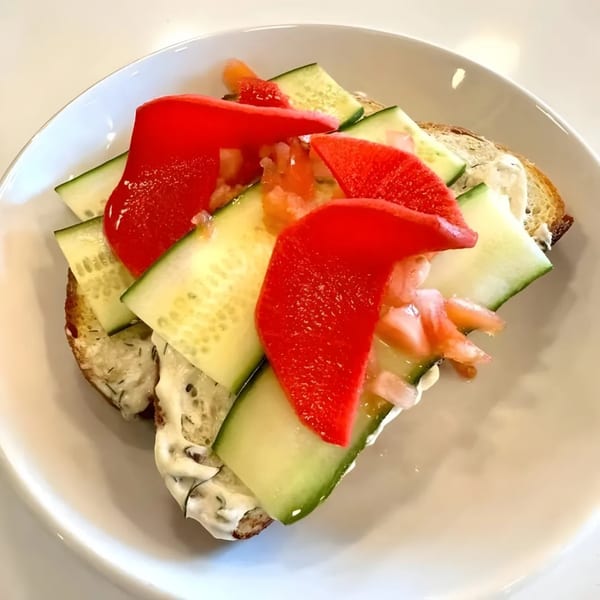 Brunch toast with cream cheese, cucumber slices, and red bell pepper on a white plate.