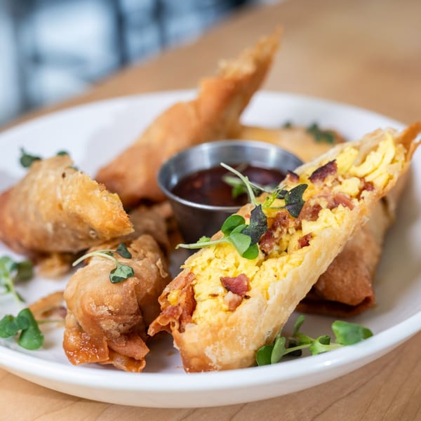 Crispy brunch egg rolls filled with scrambled eggs and bacon, served with dipping sauce.