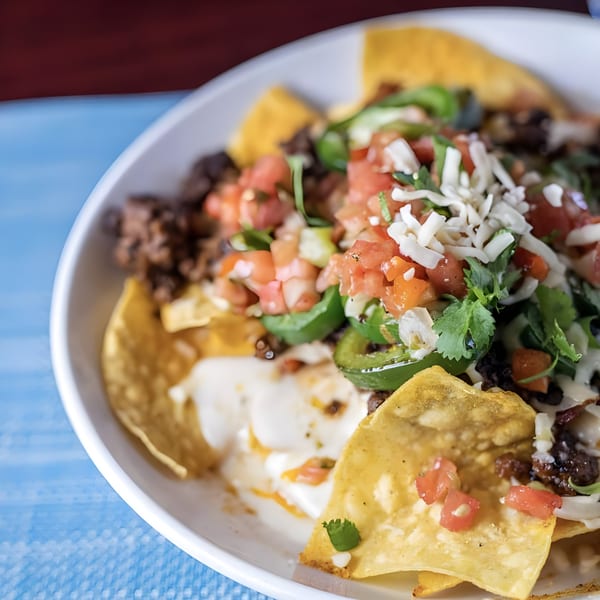 Close-up of loaded nachos with melted cheese, ground meat, pico de gallo, jalapeños, and cilantro.