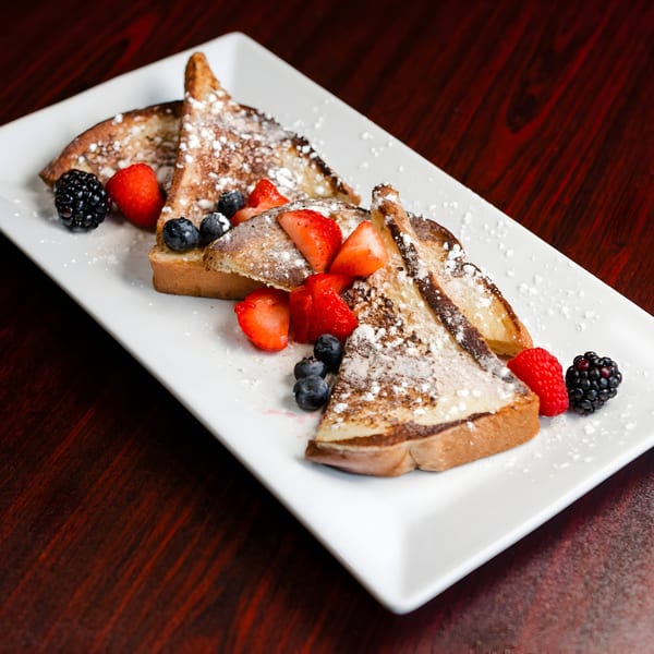 French toast triangles dusted with powdered sugar, topped with fresh strawberries, blueberries, raspberries, and blackberries.