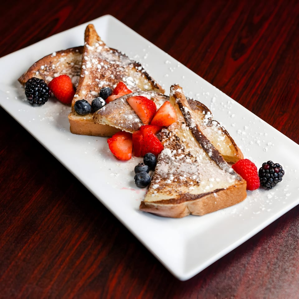 French toast triangles dusted with powdered sugar, topped with fresh strawberries, blueberries, raspberries, and blackberries.