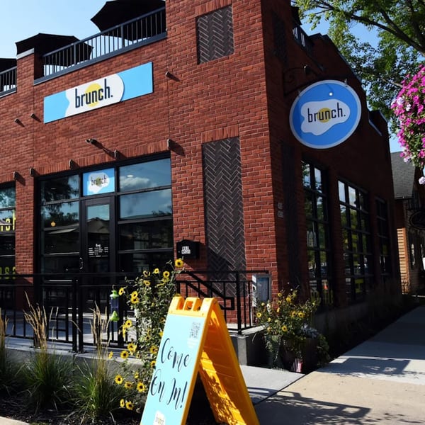Exterior of Brunch restaurant with brick facade, large windows, and a "Come On In!" sign.