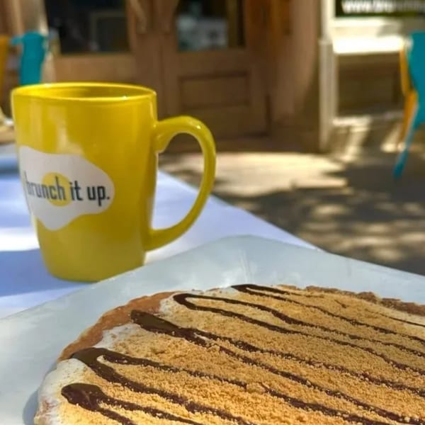A yellow "Brunch it up" mug next to a dessert pizza with chocolate drizzle and graham cracker crumbs.