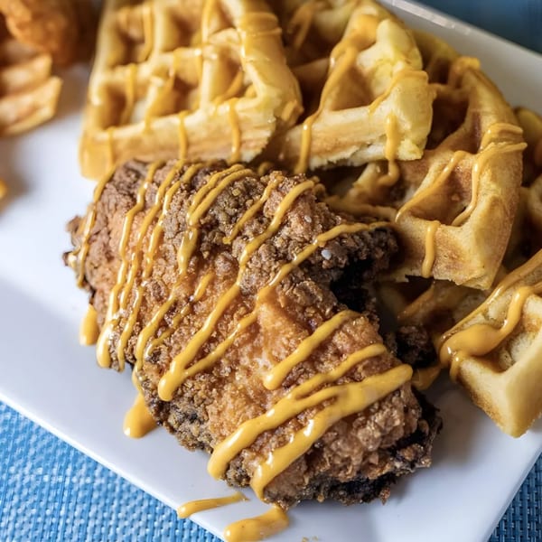 Crispy fried chicken and waffles drizzled with a golden sauce on a white plate.