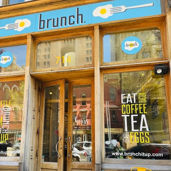 The exterior of Brunch. restaurant, featuring a blue sign with a fried egg and fork logo.