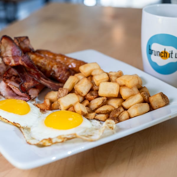 A Brunch It Up breakfast plate with fried eggs, bacon, ham, sausages, and home fries.