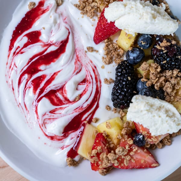 A close-up of a yogurt bowl with raspberry swirl, granola, strawberries, blueberries, blackberries, and pineapple.