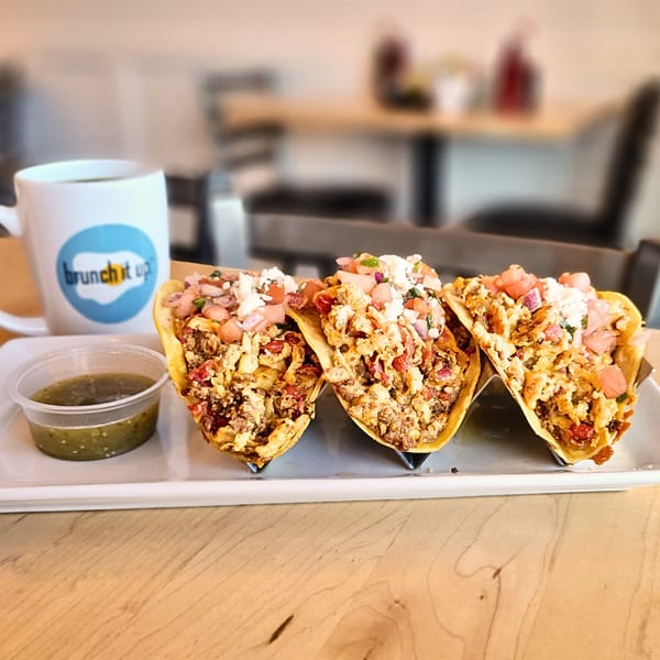 Three breakfast tacos with scrambled eggs, cheese, and salsa, with a coffee mug and green salsa.