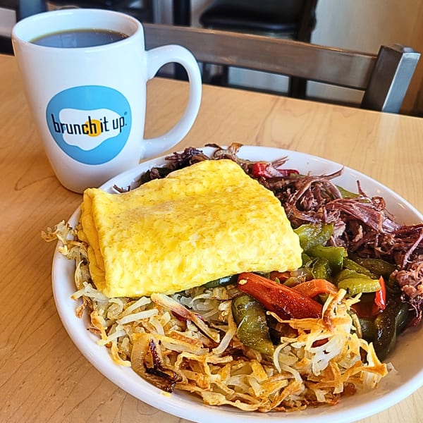 A Brunch It Up mug and a plate of hash browns, omelet, shredded beef, and peppers.