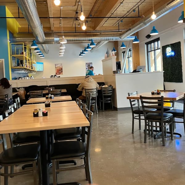 Interior of Brunch. restaurant with light wood tables, black chairs, and blue pendant lights.